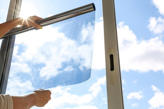 Two hands of a man opening a tint film in front of a window for making a window tinting service